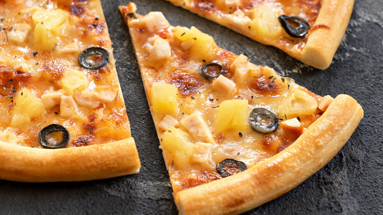 A Hawaiian pizza with black olives on it