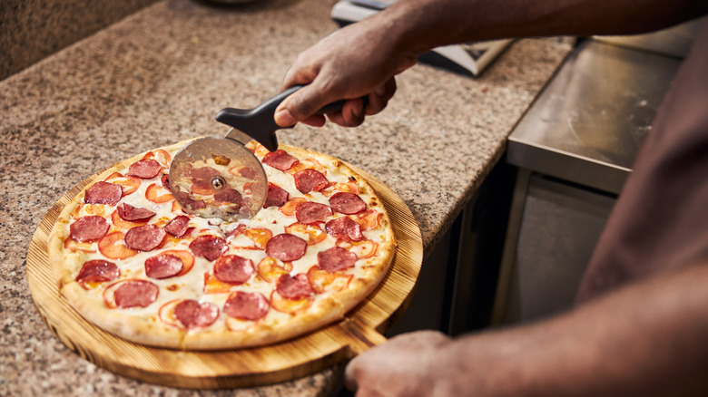 A person slicing pizza with a pizza cutter 