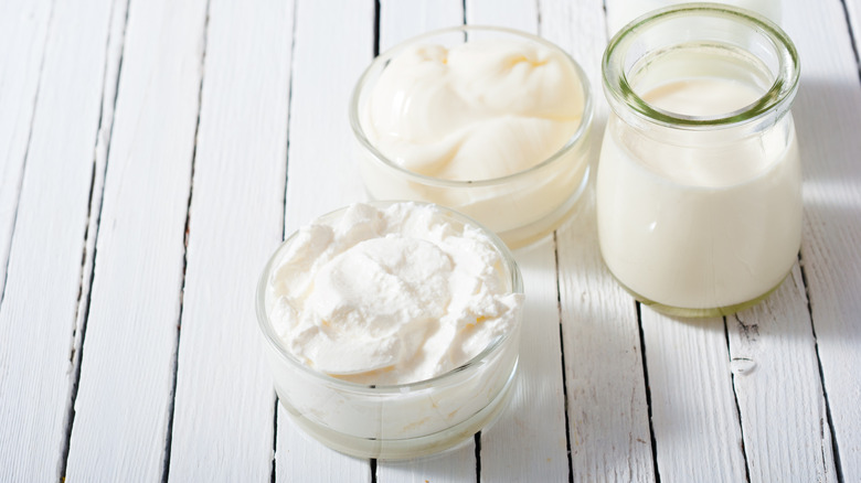 Jars of heavy cream, creme fraiche, and whipped cream on a white table