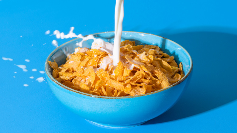 cornflakes in blue bowl, milk being poured on cereal