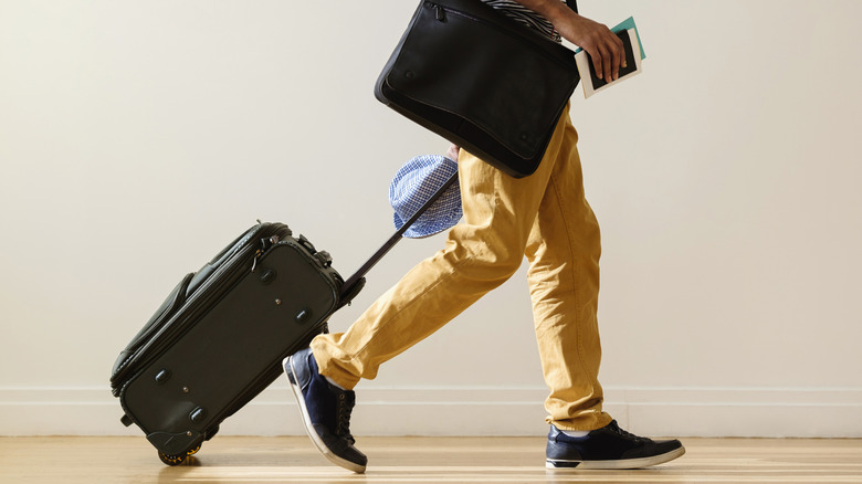 Man holding passport and pulling carry-on bag