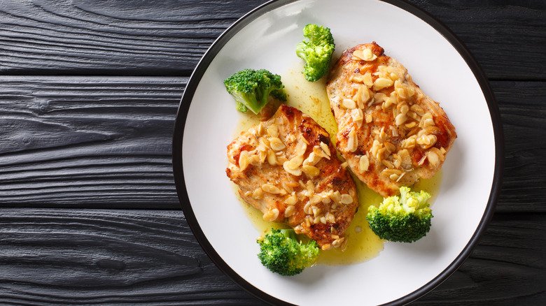 chicken breasts with almonds and broccoli on white plate