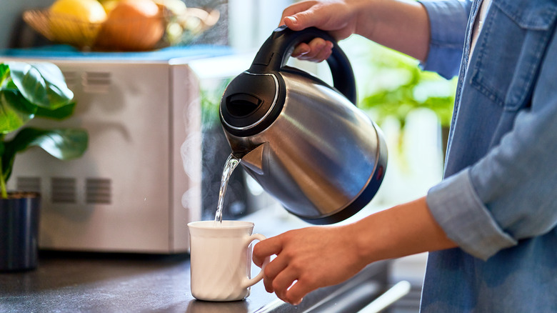 Hands pouring boiling water on a white cup