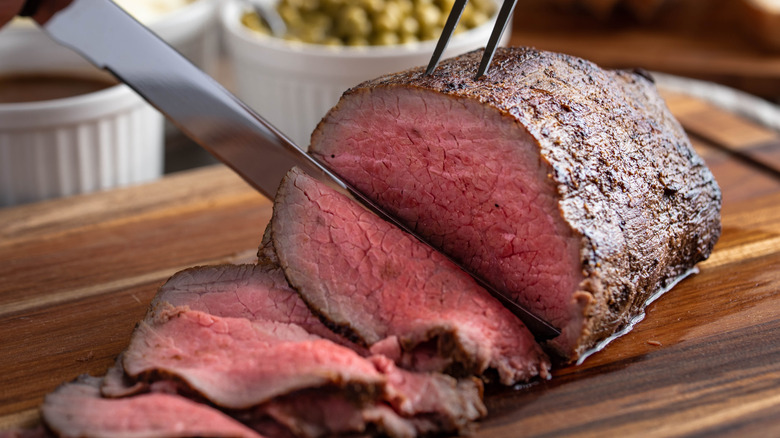 Slicing roast beef with a knife on a cutting board