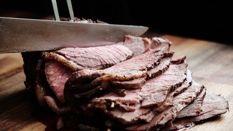 Using a knife to cut roast beef against the grain on a wood board