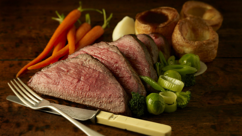 Sliced roast beef with veggies and cutlery on a wooden board