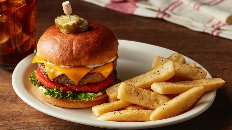 Hamburger and French fries on white plate on brown wooden table.