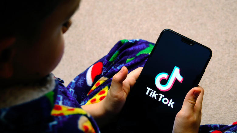 Child holding smartphone displaying TikTok logo