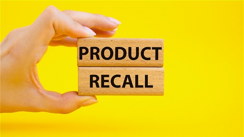 Hand holding "product recall" blocks yellow background