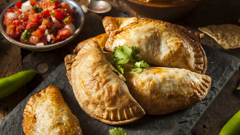 homemade crispy baked empanadas stacked on a slate board with a bowl of salsa