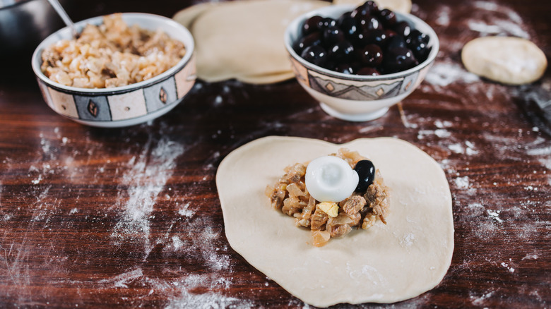 empanada dough topped with filling and ingredients in background