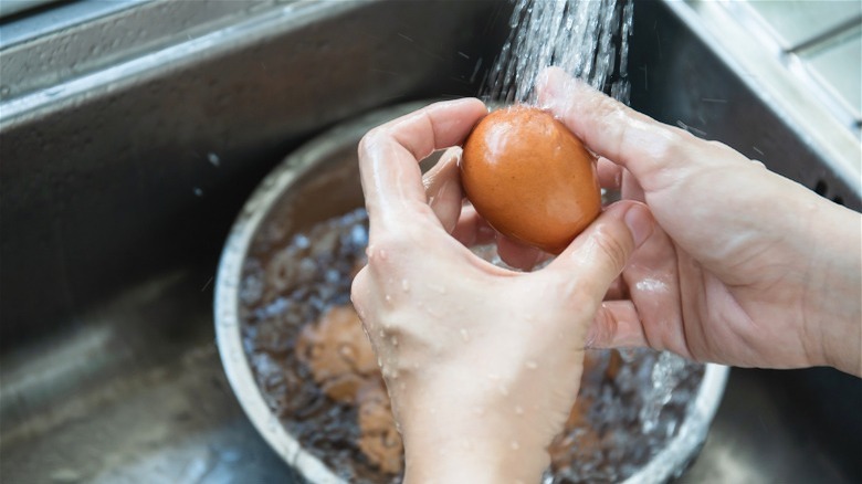 Hands holding brown egg in sink under running water