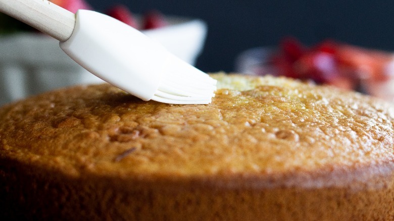 simple syrup is being brushed on a vanilla cake