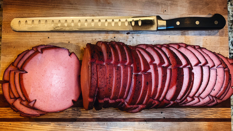 sliced glazed smoked bologna log with slicing knife