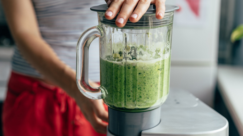 person making green smoothie in blender