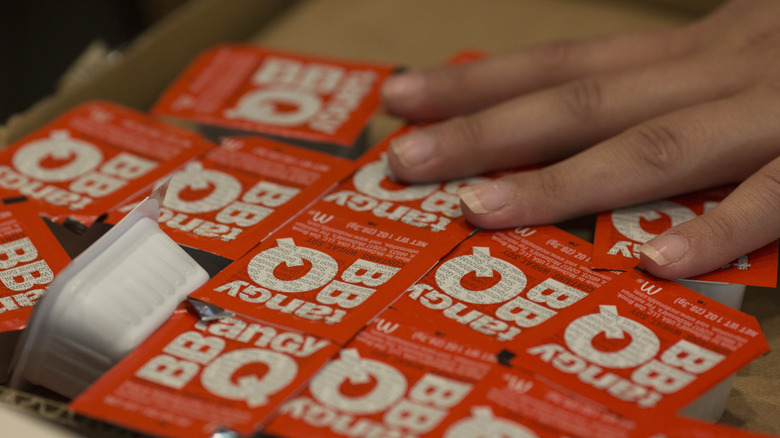 McDonald's tangy BBQ sauce containers in box with employee hand on top