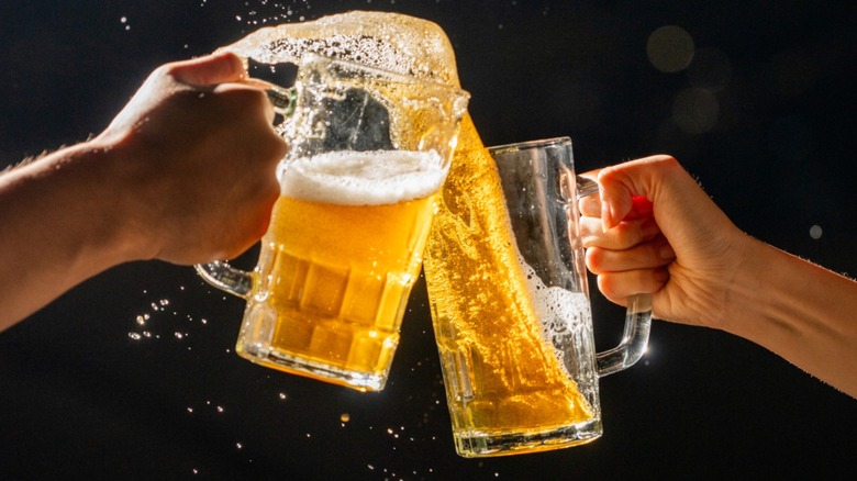 Hands tapping beer mugs together as beer splashes