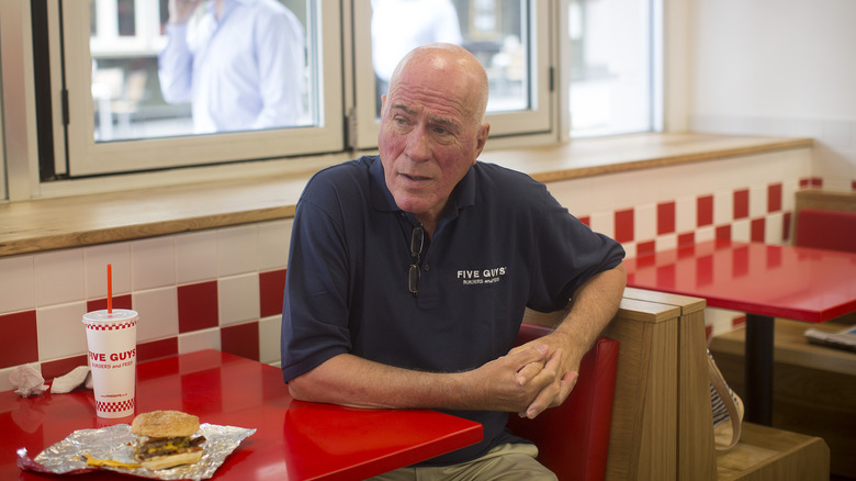 Jerry Murrell sitting in a Five Guys booth with a burger and drink in front of him