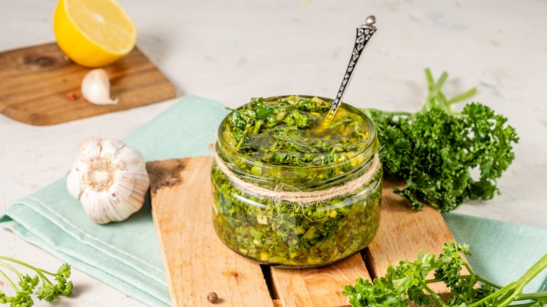 Chimichurri in a small glass jar with a spoon in it