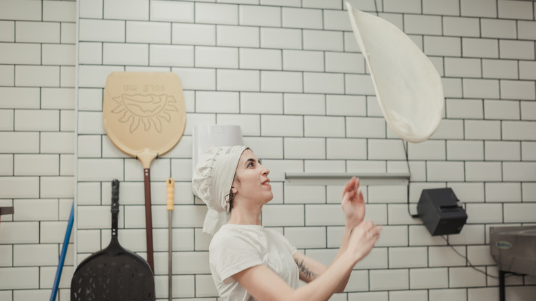 A pizza chef tosses dough high into the air. 