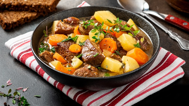 lamb stew in a black bowl on top of a tea towel