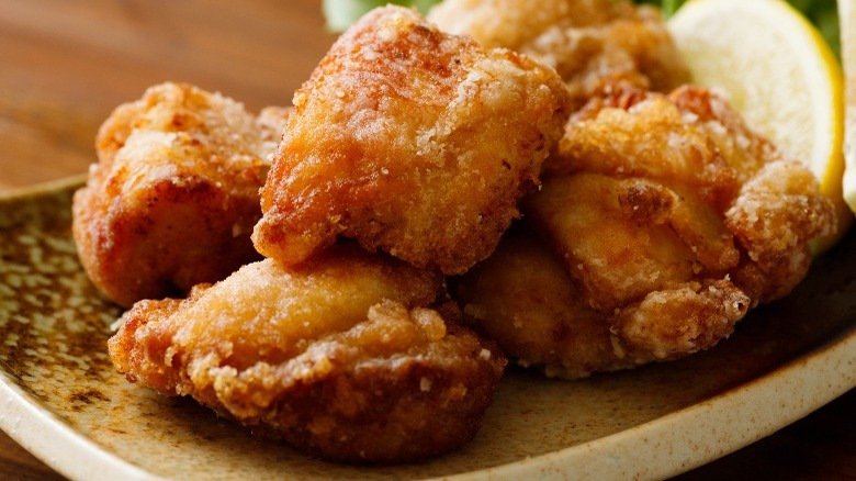 Pieces of karaage on a black plate with a lemon wedge