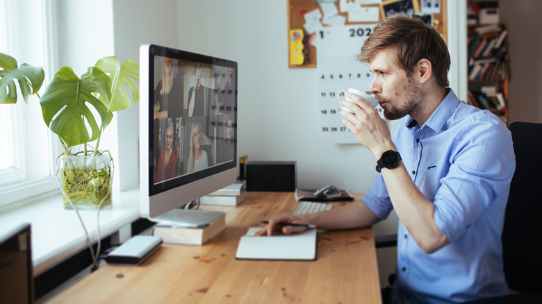 Man drinking mug of coffee at computer desk