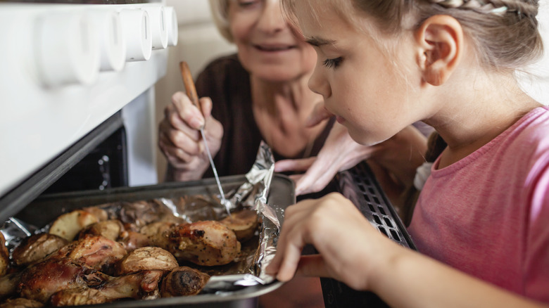 woman and girl putting chicken in oven