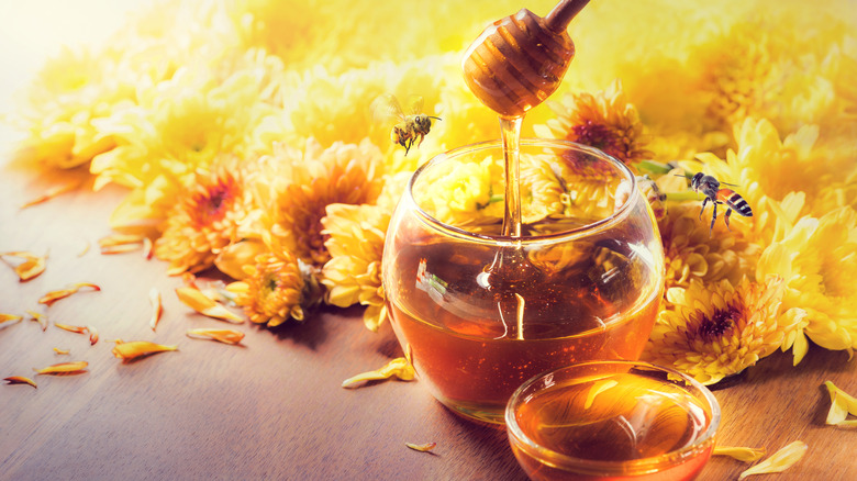 Bowls of honey with dipper, bees, and flowers