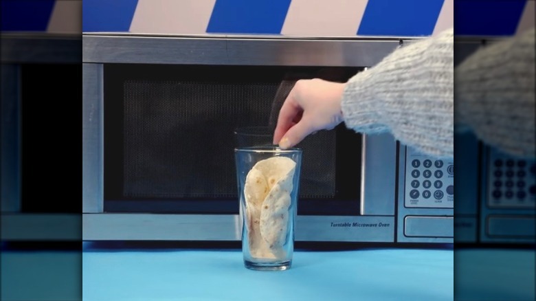 A tortilla in a glass in front of a microwave