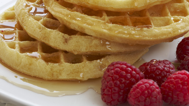 Stack of waffles with butter, syrup, and berries on white plate