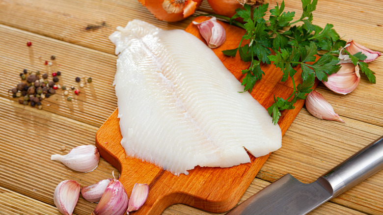 Fillet of raw halibut fish on wooden surface with garlic and greens