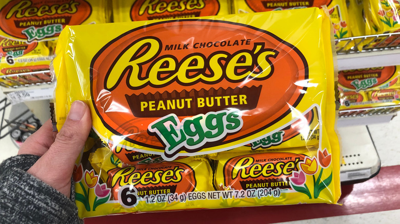 Person holding a package of Reese's peanut butter eggs in a grocery store aisle