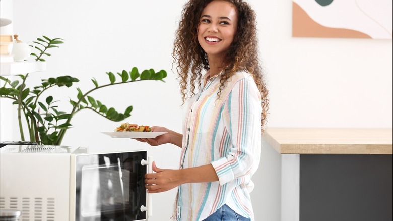 woman smiling while using microwave