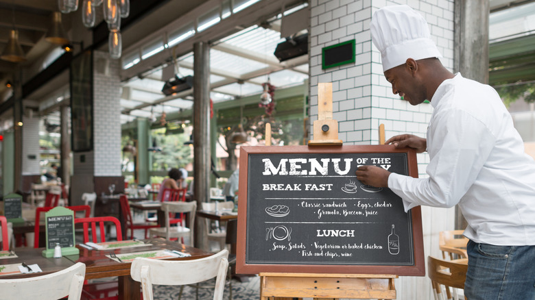 man in chef hats writes menu on blackboard