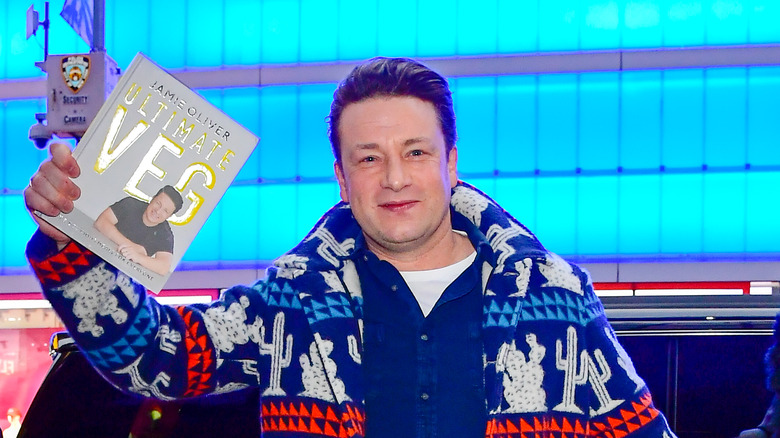 Jamie Oliver holds up his book