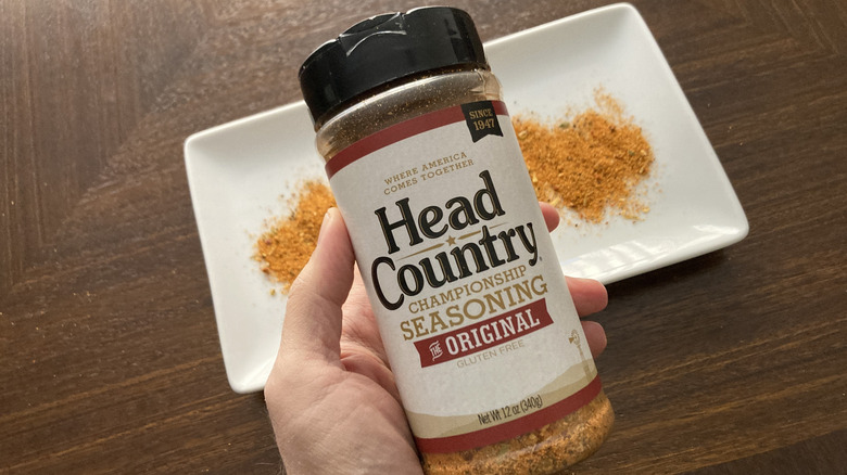 A hand holding a container of Head Country barbecue seasoning