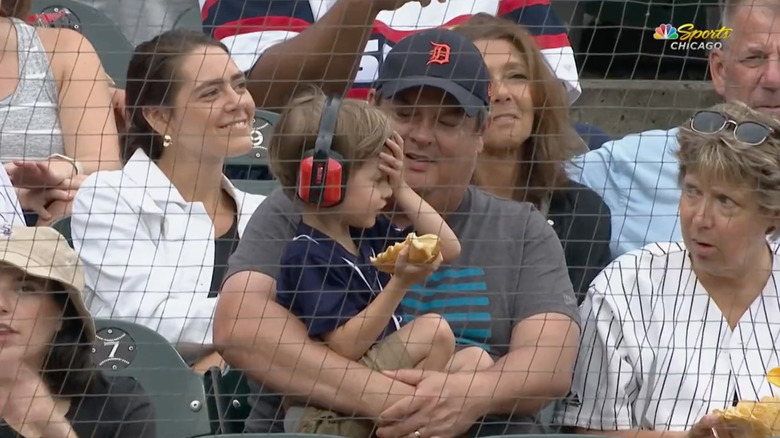 a little boy holding his face sitting at a baseball game