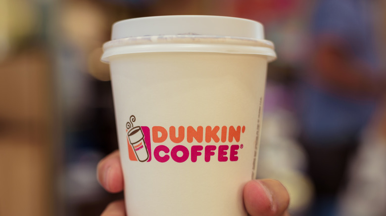 A hand holding a cup of Dunkin' coffee