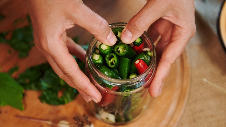 hands packing cut peppers in a jar