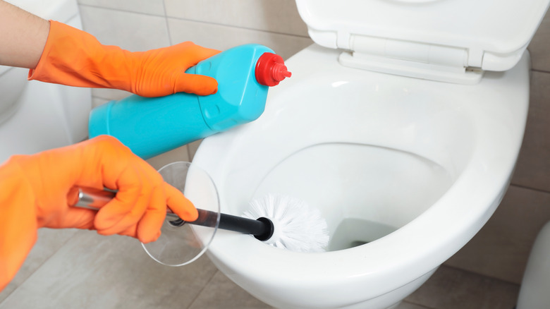 Person wearing orange gloves scrubbing toilet bowl