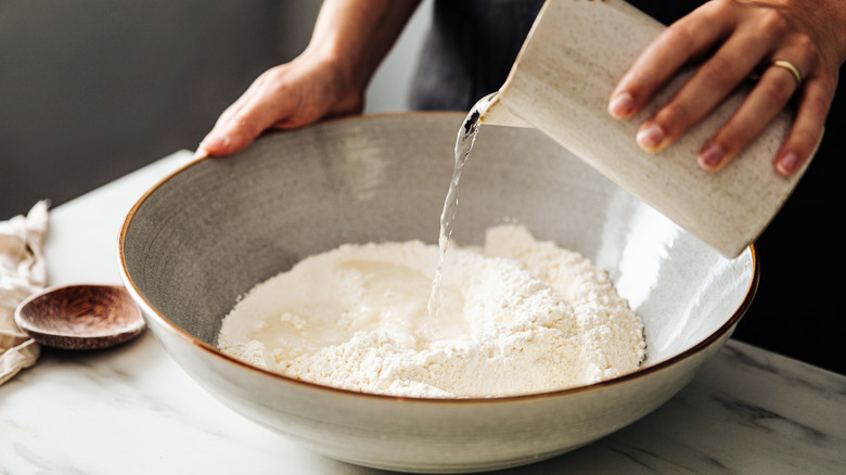 Person pouring water into flour