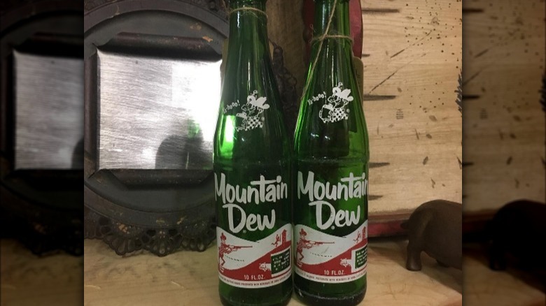 Two vintage bottles of Mountain Dew with early art work depicting a shoe-less hillbilly with a shotgun