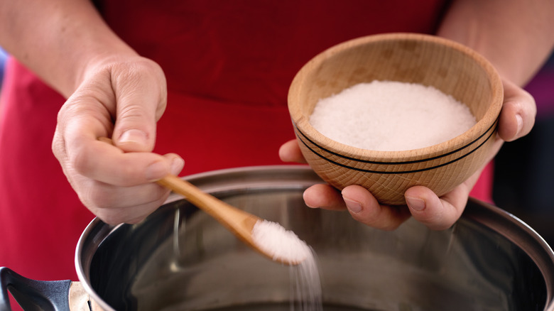 someone spooning salt into a pan