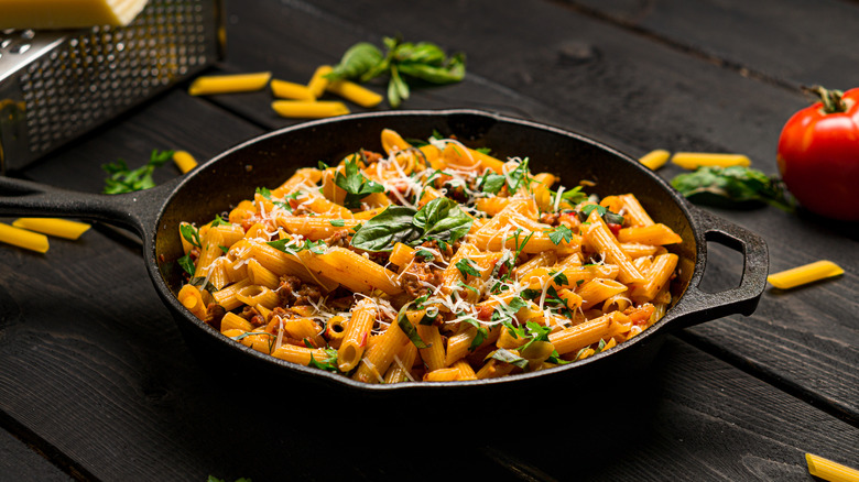 Skillet of pasta and assorted ingredients on black table