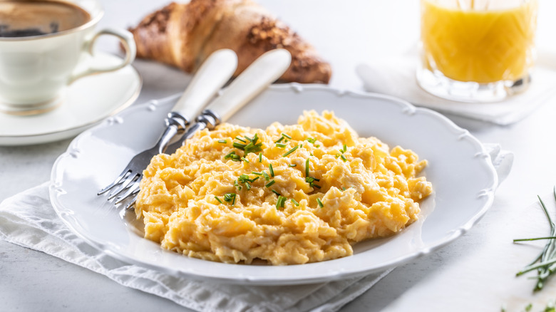 fluffy and creamy scrambled eggs on a fancy plate with coffee and orange juice in the background