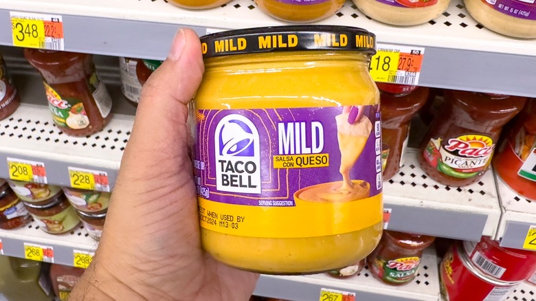 A person holds a jar of Taco Bell salsa con queso at the grocery store