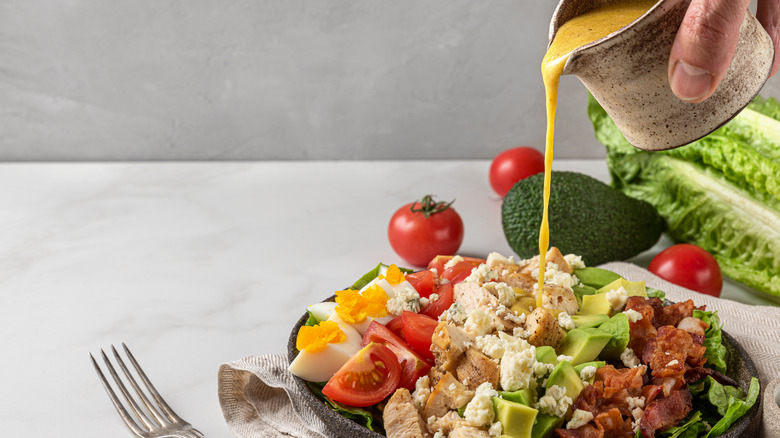 Man pours salad dressing onto salad