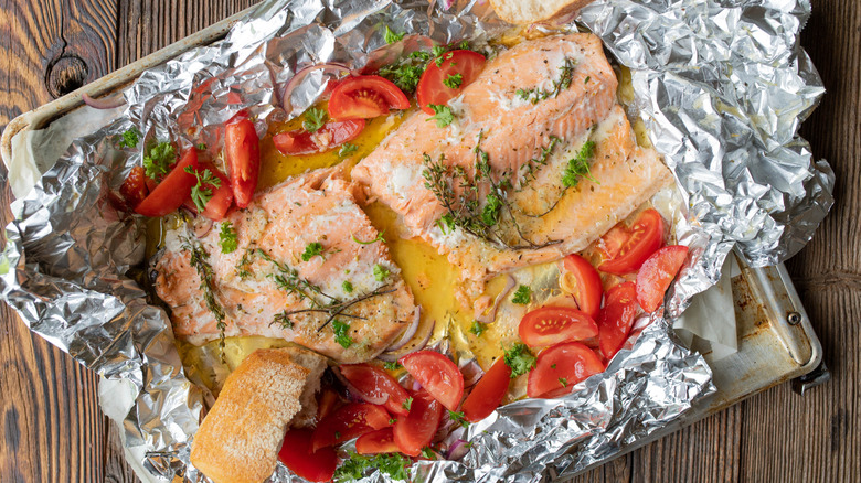 Salmon with vegetables and herbs on a foil-lined baking pan