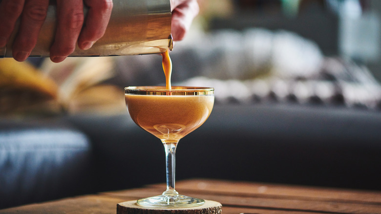 hands pouring cocktail shaker into glass